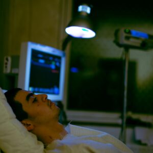 A patient lying in a hospital bed with medical monitors and lighting.